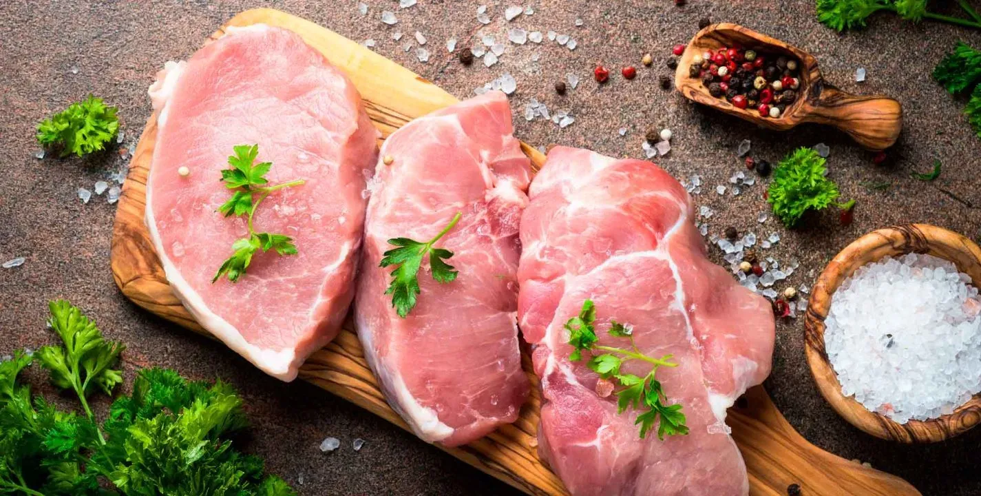 Cortes de carne de cerdo fresca con hierbas y especias en tabla de madera.